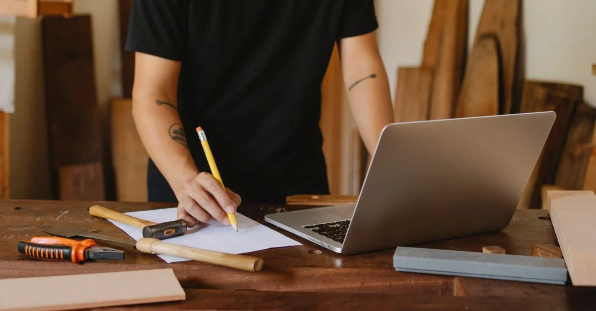 Un artisan planifiant des projets sur un ordinateur portable au milieu des outils dans un studio de travail du bois.