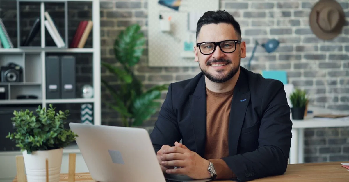 Homme d'affaires en lunettes souriant tout en travaillant sur un ordinateur portable dans un bureau moderne.