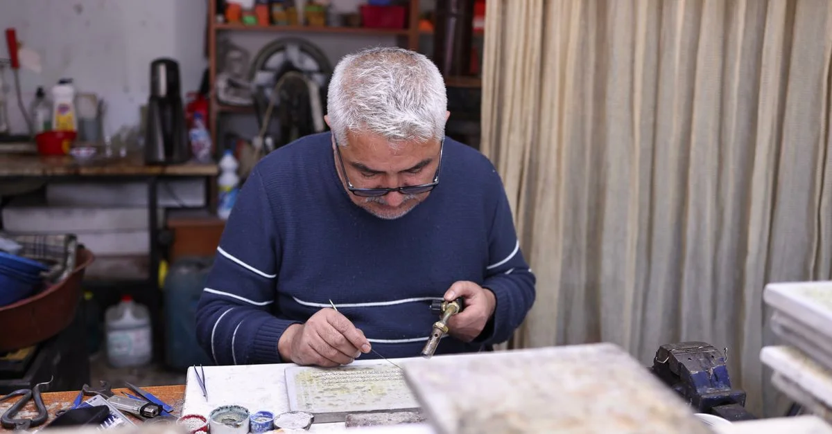 Un artisan qualifié travaille avec soin sur des objets d'art en métal dans un atelier chaleureux.