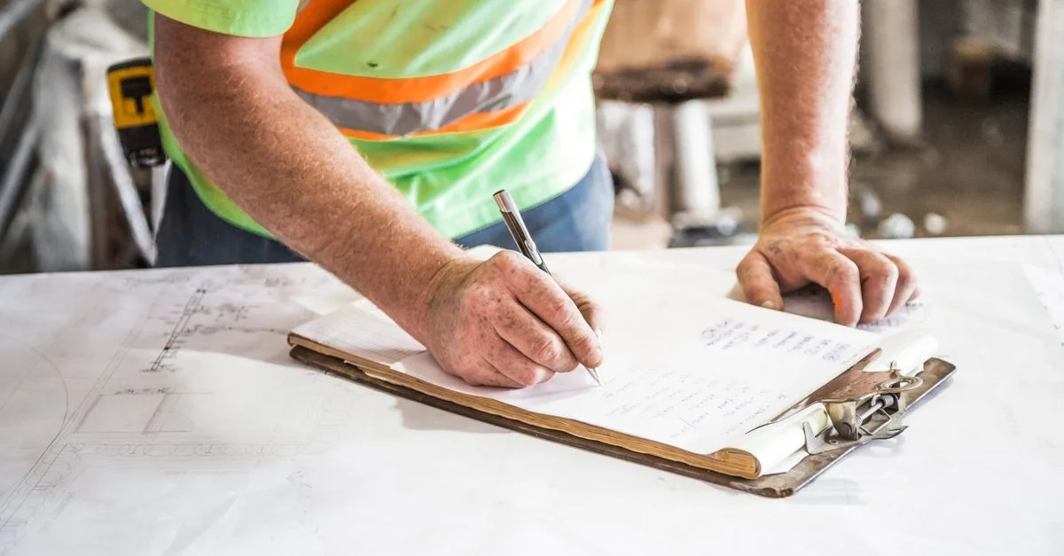 Un ouvrier du bâtiment prend des notes sur un tableau de bord sur un chantier, mettant en avant la planification et la précision.