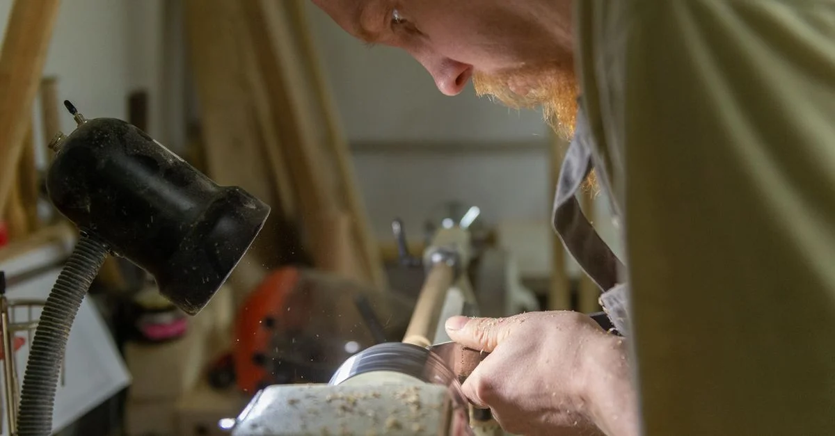 Un artisan façonne habilement du bois sur un tour sous un éclairage d'atelier ciblé.