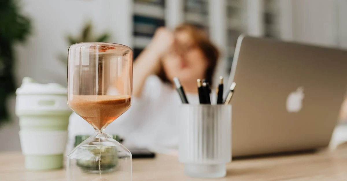 Un sablier concentré sur un bureau avec un ordinateur portable dans un cadre de bureau, mettant en avant la gestion du temps.