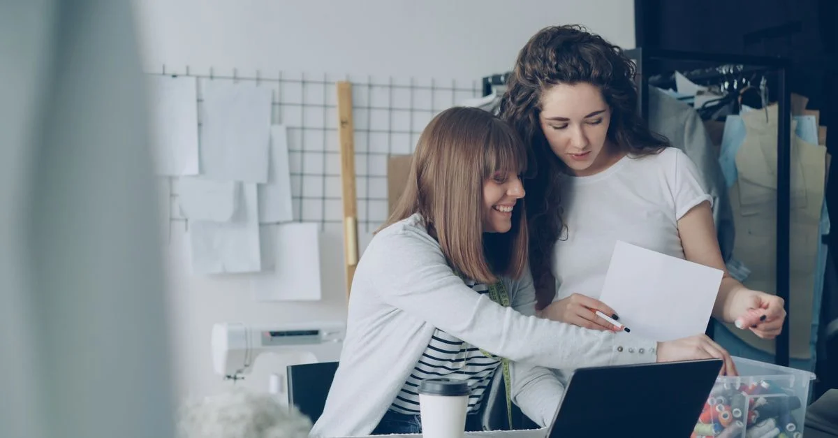 Deux femmes collaborant dans un espace de bureau moderne, partageant des idées et révisant des designs.